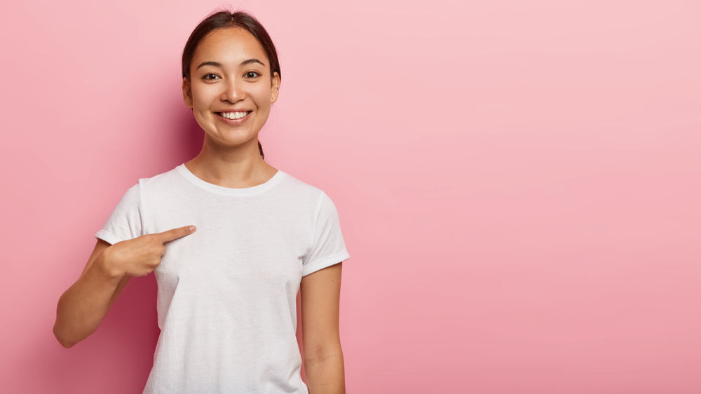 Happy,Smiling,Asian,Woman,Points,At,Plain,White,T,Shirt,