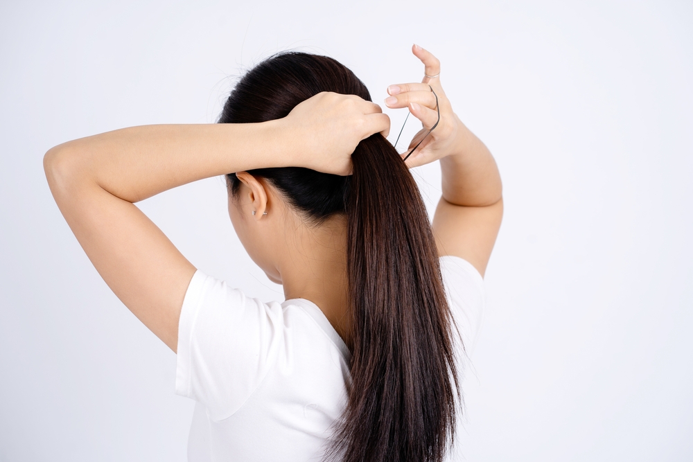 Asian,Woman,Tying,Her,Hair,Up,Isolated,On,A,White