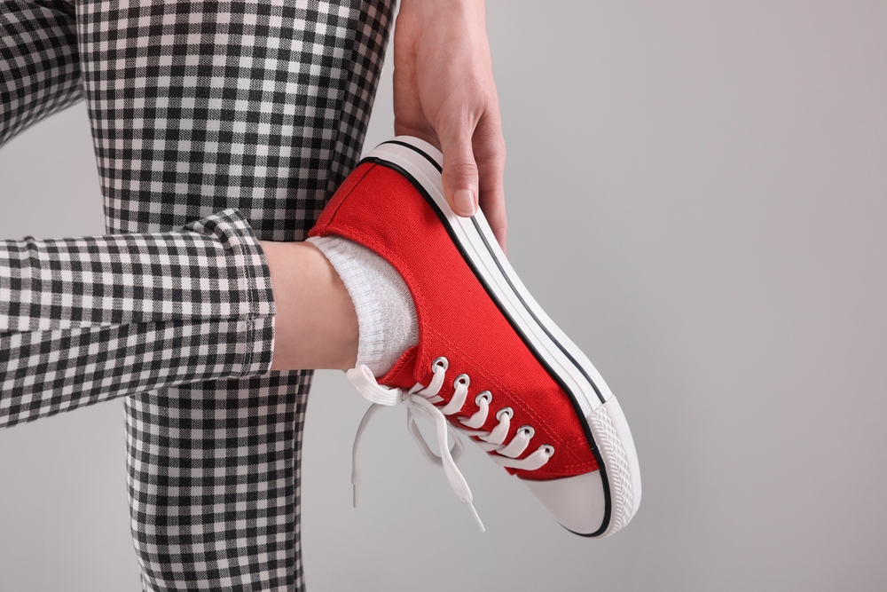 Woman,Putting,On,Red,Classic,Old,School,Sneaker,Against,Light