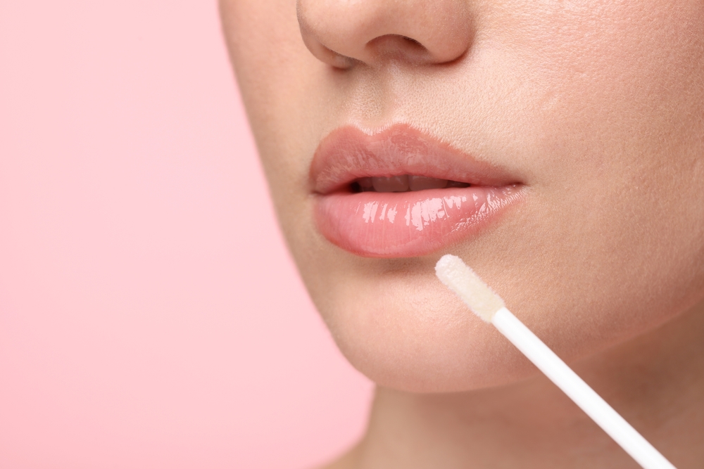 Woman,Applying,Lip,Gloss,On,Pink,Background,,Closeup.,Space,For